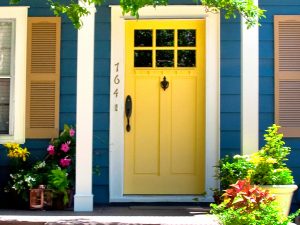 Blue house exterior with yellow door, new windows, flowers, plants, and covered porch area.